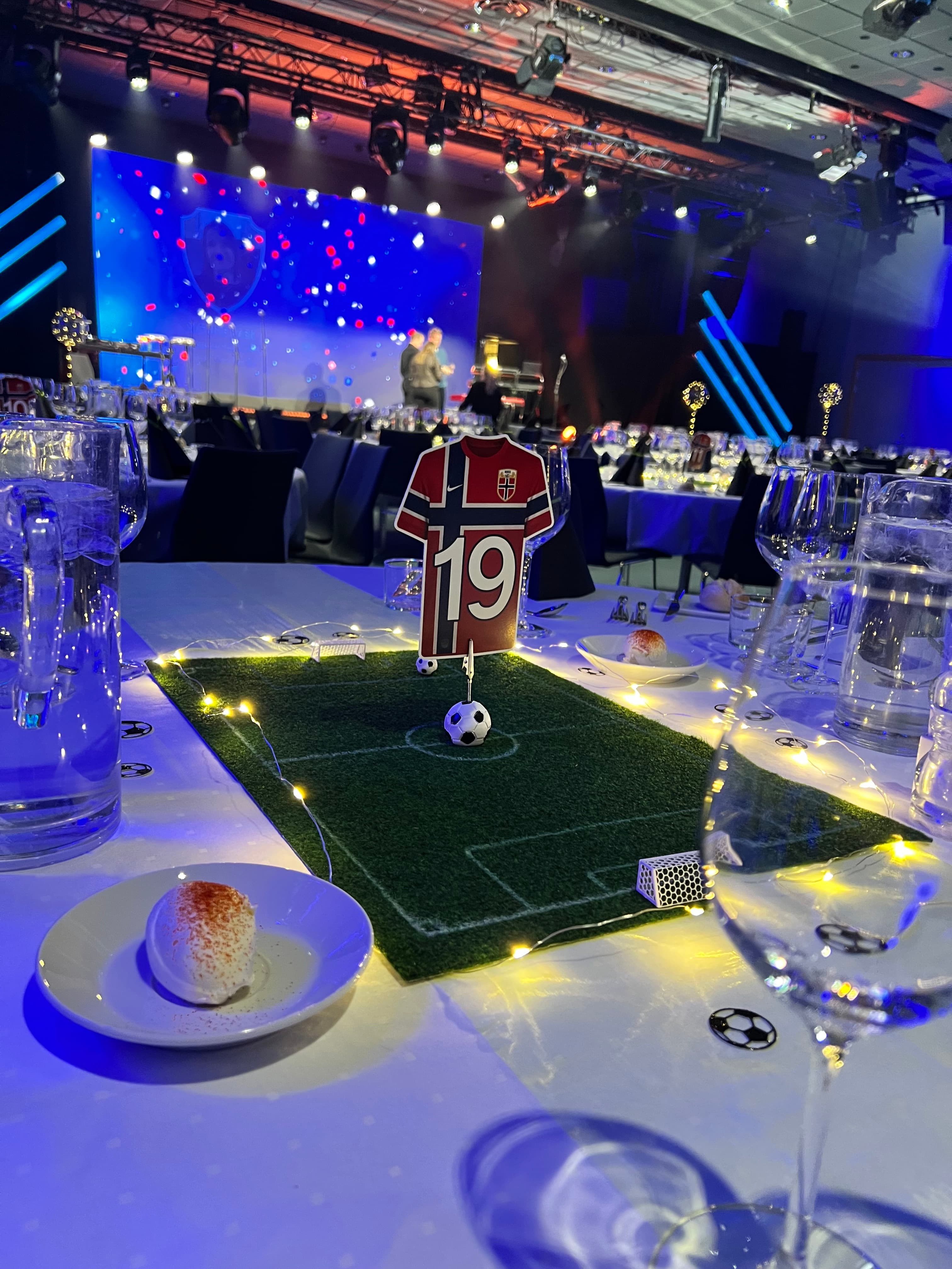 Scene med blå lyssetting og spesialgrafikk for fotballmiddag.
