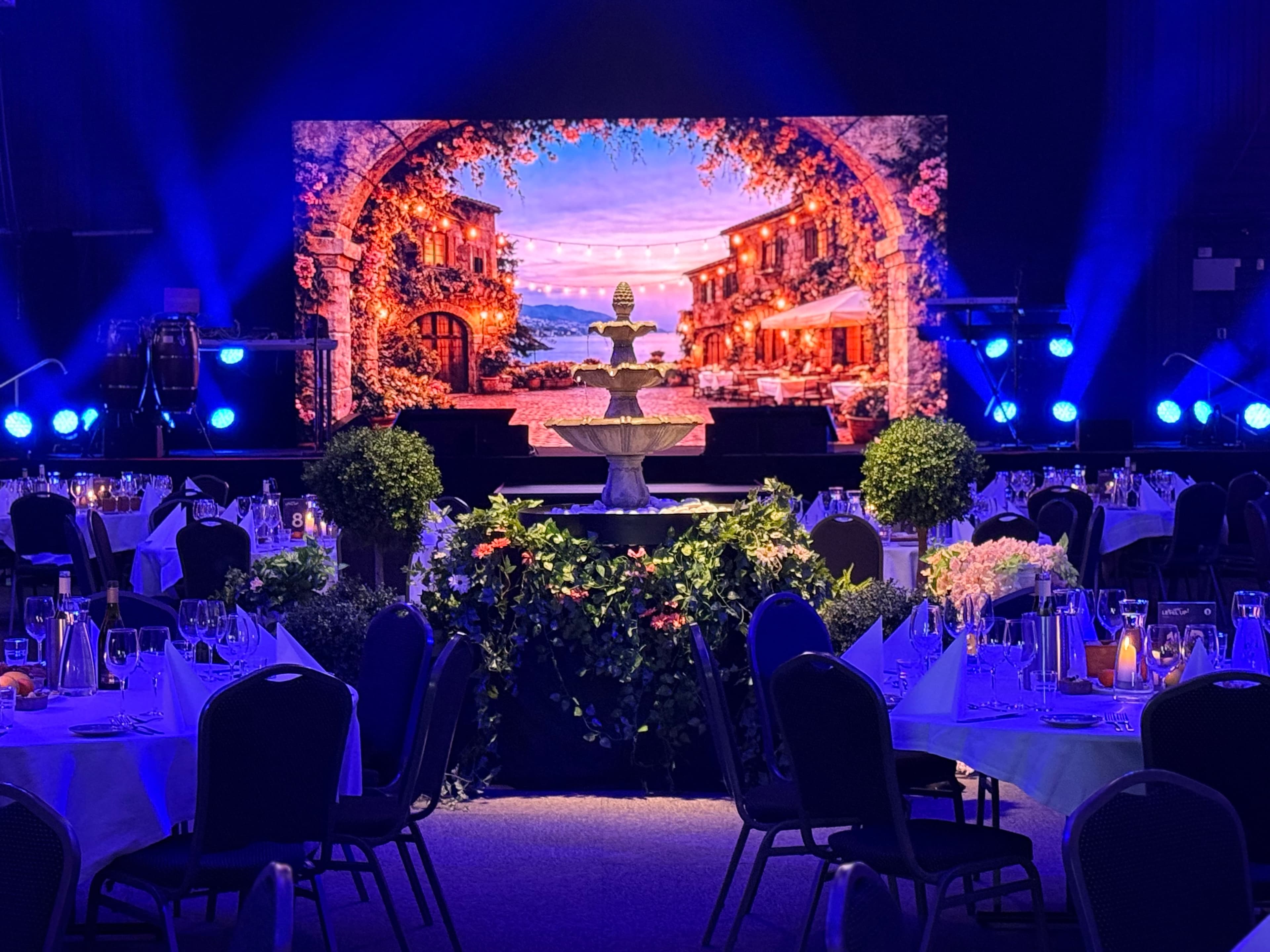 Middelhavsinspirert eventrom med scenografi, fontene og dekket middagssal.