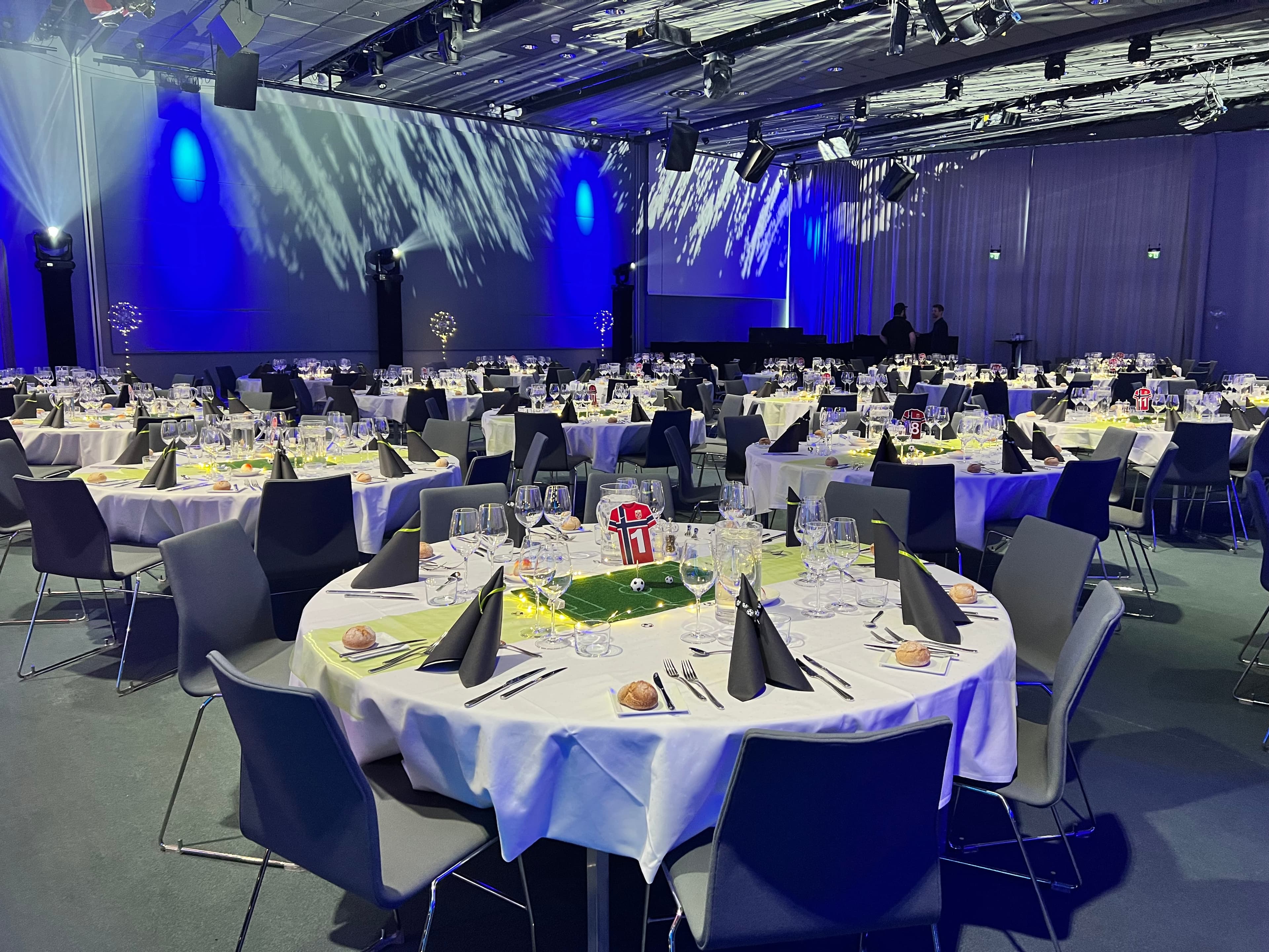 Fotballmiddag med gjennomført bordkonsept, minibaner og blå lyssetting.